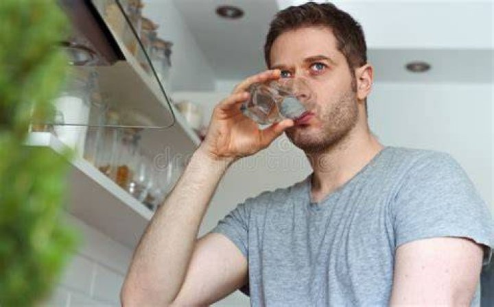 Unshaven man drinks water from a glass in the kitchen. unshaven man drinks water from a glass in the kitchen